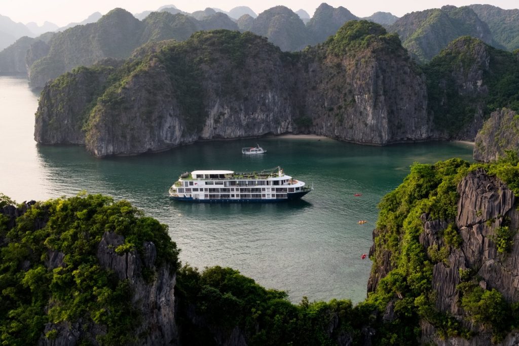 Scenic view of a luxury cruise boat sailing through emerald waters surrounded by towering limestone.