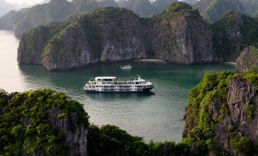 Scenic view of a luxury cruise boat sailing through emerald waters surrounded by towering limestone.