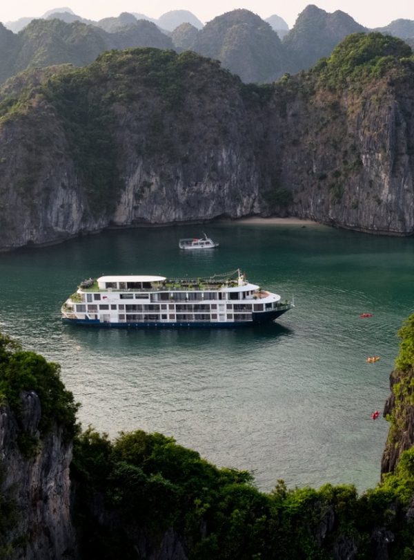Scenic view of a luxury cruise boat sailing through emerald waters surrounded by towering limestone.