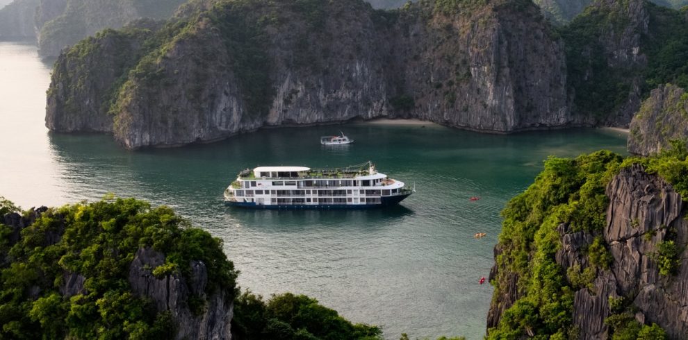Scenic view of a luxury cruise boat sailing through emerald waters surrounded by towering limestone.