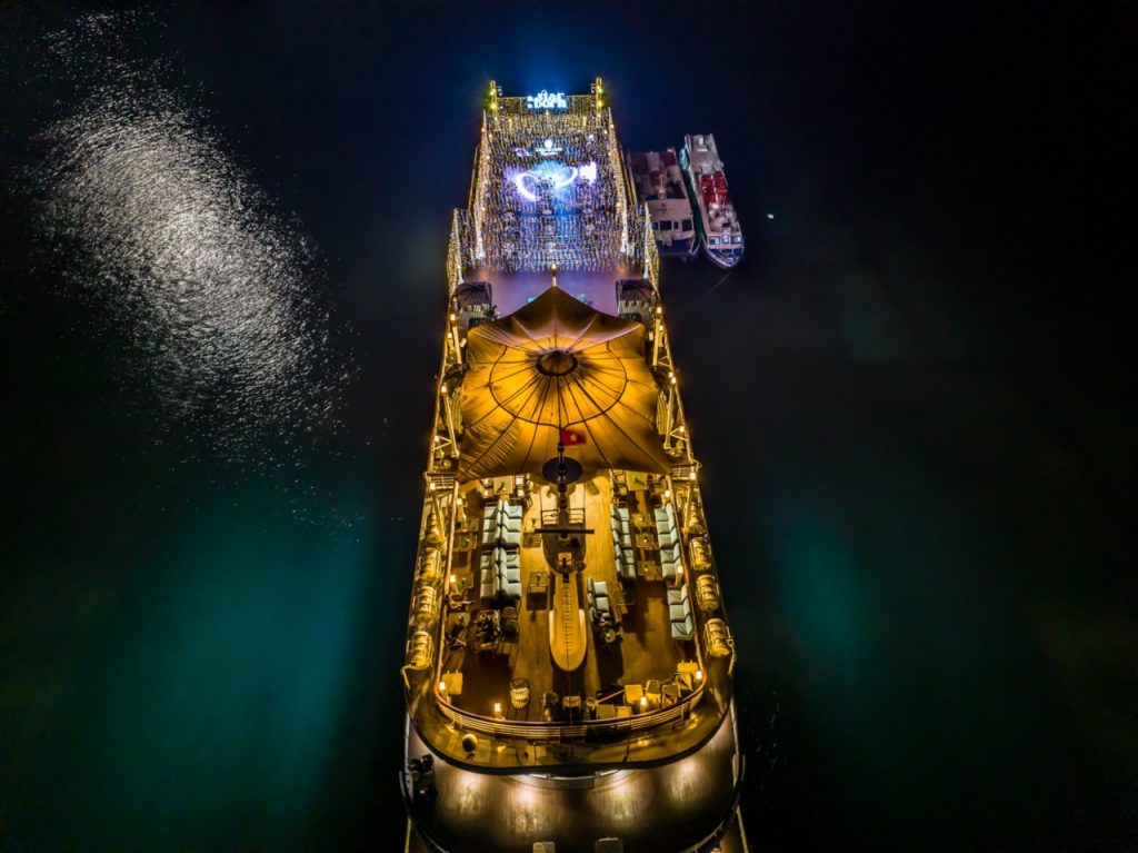 Night view of luxury cruise in Halong Bay with illuminated deck and calm waters, perfect for a sceni.