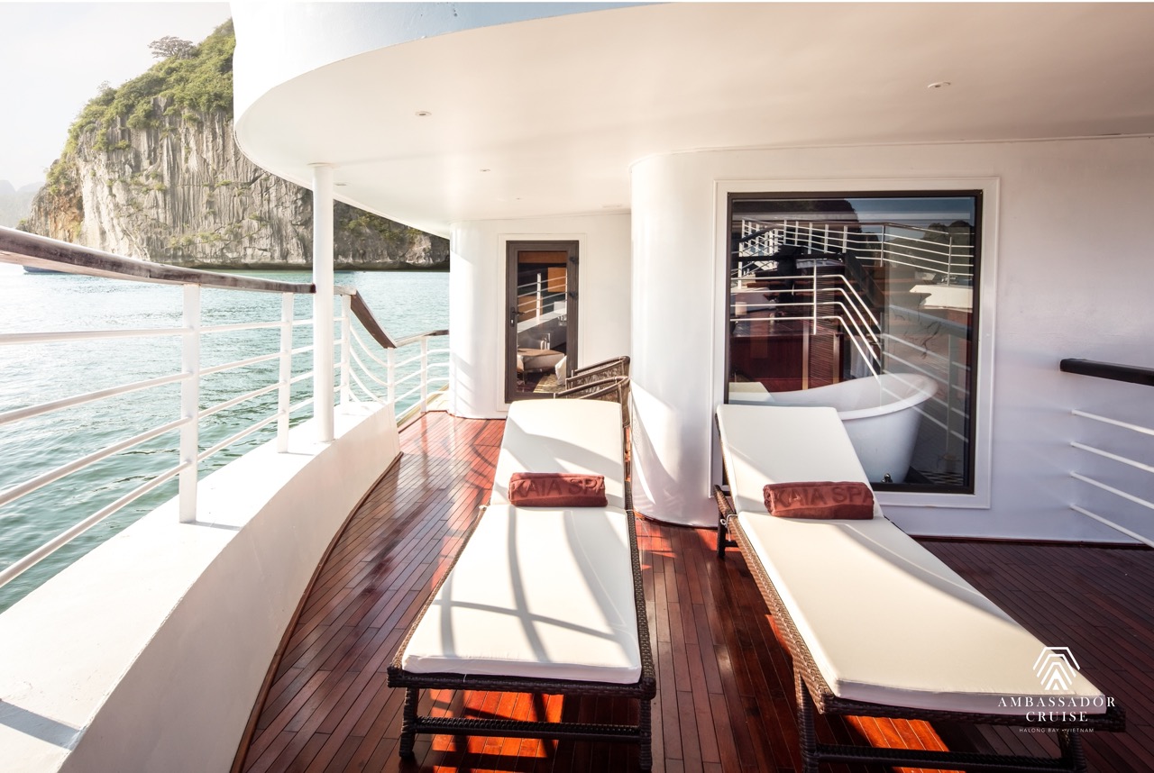Stunning view from cruise balcony in Halong Bay with relaxing lounge chairs and clear blue waters.