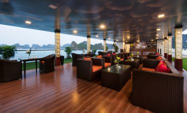 Spacious cruise lounge with panoramic views of Halong Bay, elegant seating, and relaxing ambiance.