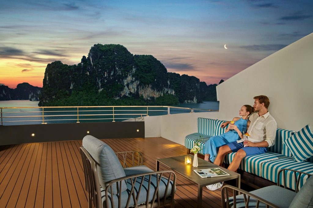 Relaxing couple on a sunset cruise in Ha Long Bay, Vietnam, with stunning limestone karsts and ocean views.
