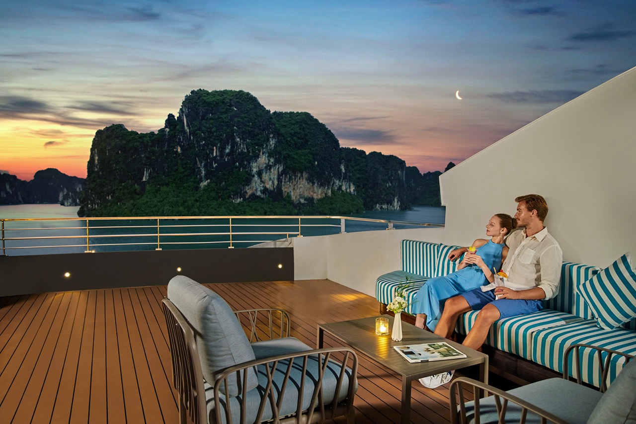 Relaxing couple on a sunset cruise in Ha Long Bay, Vietnam, with stunning limestone karsts and ocean views.