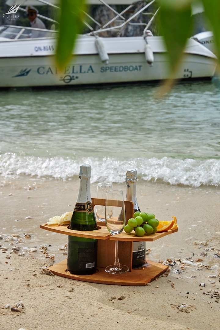 Luxury beachside champagne with grapes and orange slices on sandy shore, boat in background.