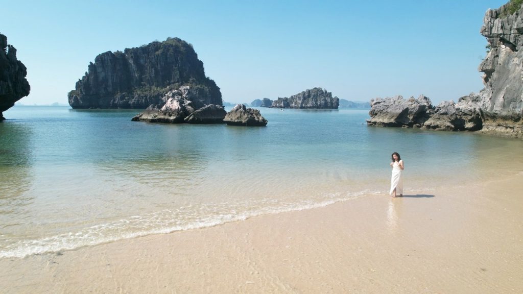 Seaside breathtaking view with rocks and clear water, woman in white dress enjoying beach scenery.