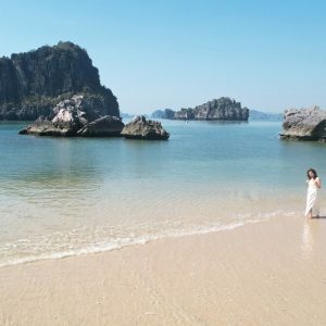Seaside breathtaking view with rocks and clear water, woman in white dress enjoying beach scenery.