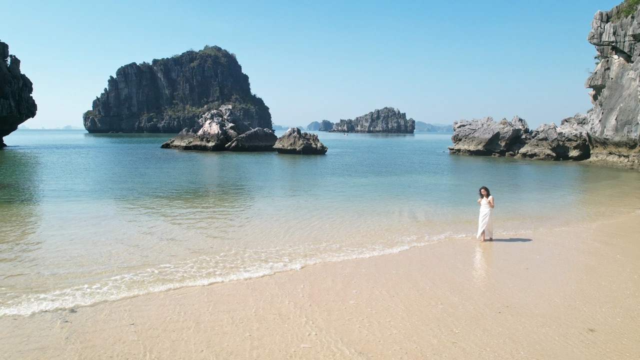 Seaside breathtaking view with rocks and clear water, woman in white dress enjoying beach scenery.