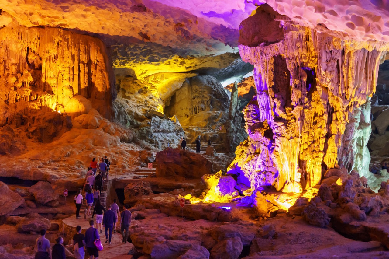 Vivid cave interior with colorful lighting and visitors exploring the stunning formations.