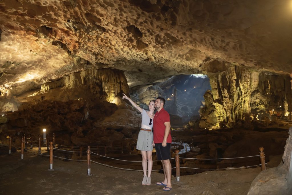 Brightly lit cave with tourists exploring underground stalactites and stalagmites in Vietnam.