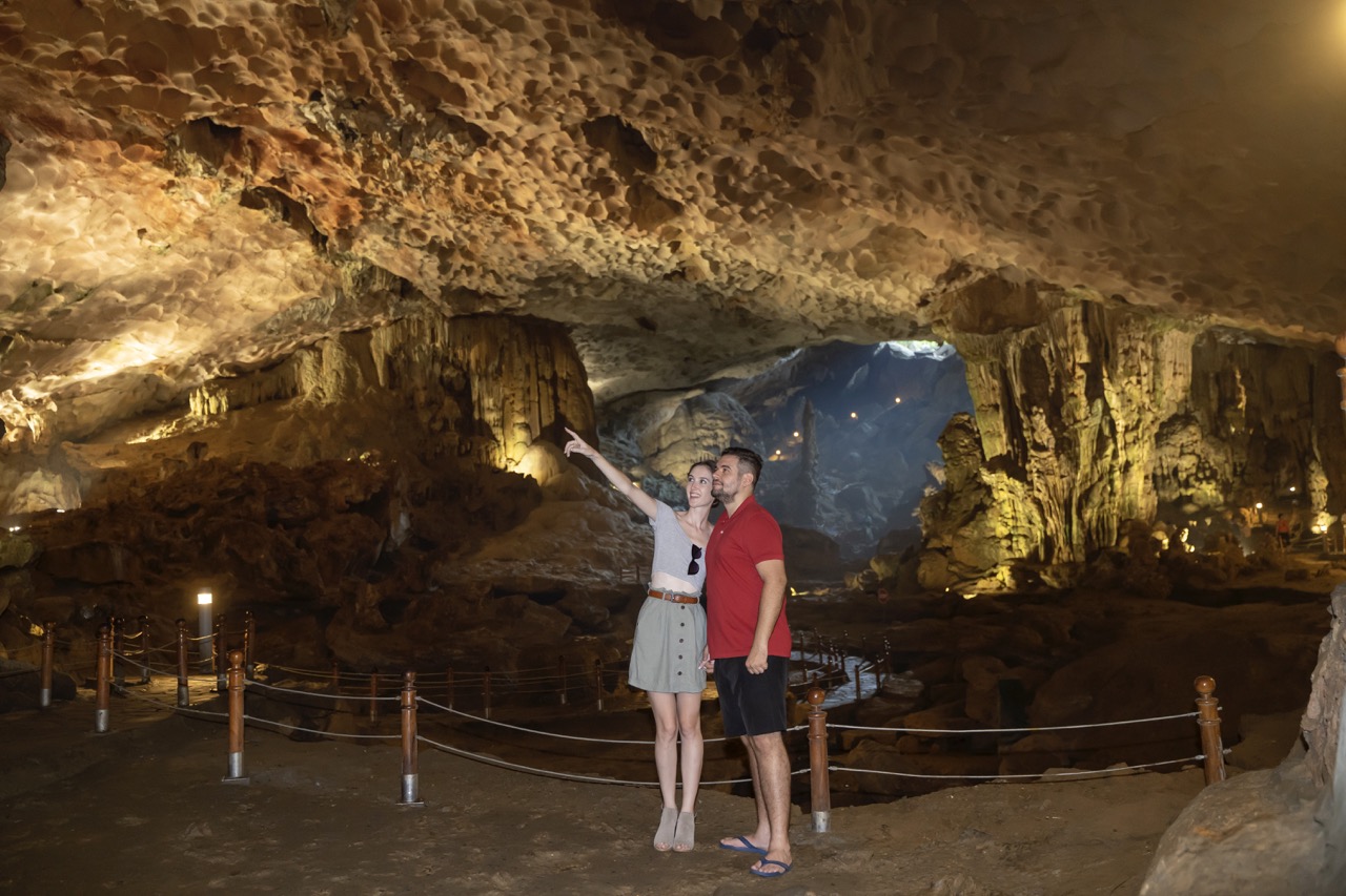 Brightly lit cave with tourists exploring underground stalactites and stalagmites in Vietnam.