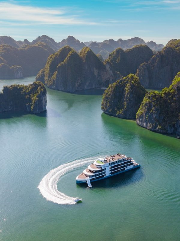 Spectacular boat cruising through emerald waters amidst towering limestone islands in Ha Long Bay, Vietnam.
