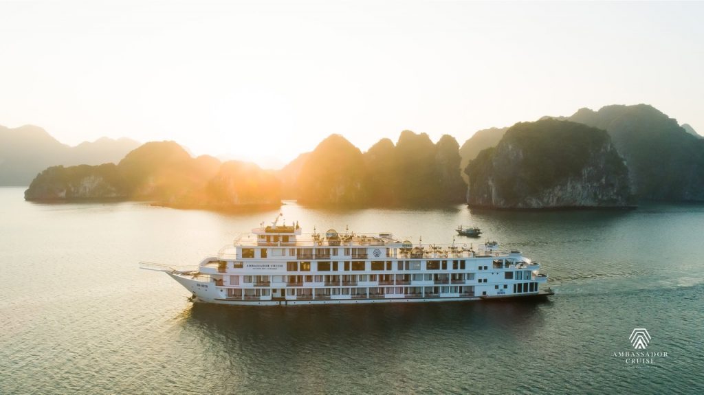 Cruise ship sailing in Halong Bay at sunset with limestone karsts and calm waters.