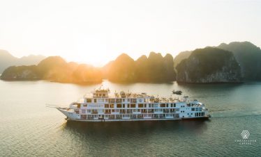 Cruise ship sailing in Halong Bay at sunset with limestone karsts and calm waters.