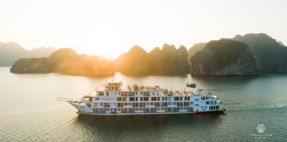 Cruise ship sailing in Halong Bay at sunset with limestone karsts and calm waters.