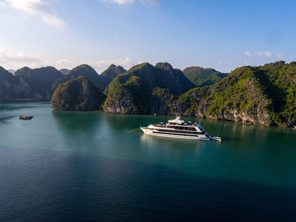Luxurious yacht sailing through emerald waters surrounded by lush green islands in Halong Bay, Vietnam.
