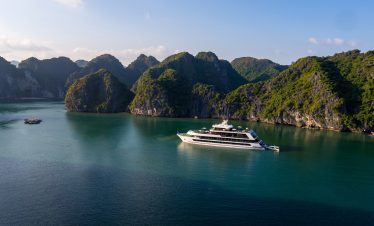Luxurious yacht sailing through emerald waters surrounded by lush green islands in Halong Bay, Vietnam.
