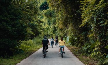 Cyclists riding through a green forest trail, enjoying nature and adventure in Halong Bay area.