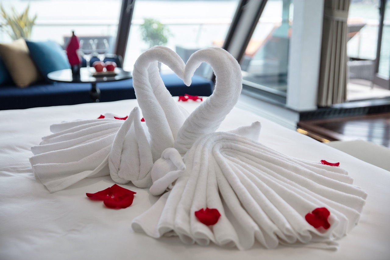 Elegant towel art of swans on a hotel bed with rose petals, perfect for romantic getaways in Vietnam.