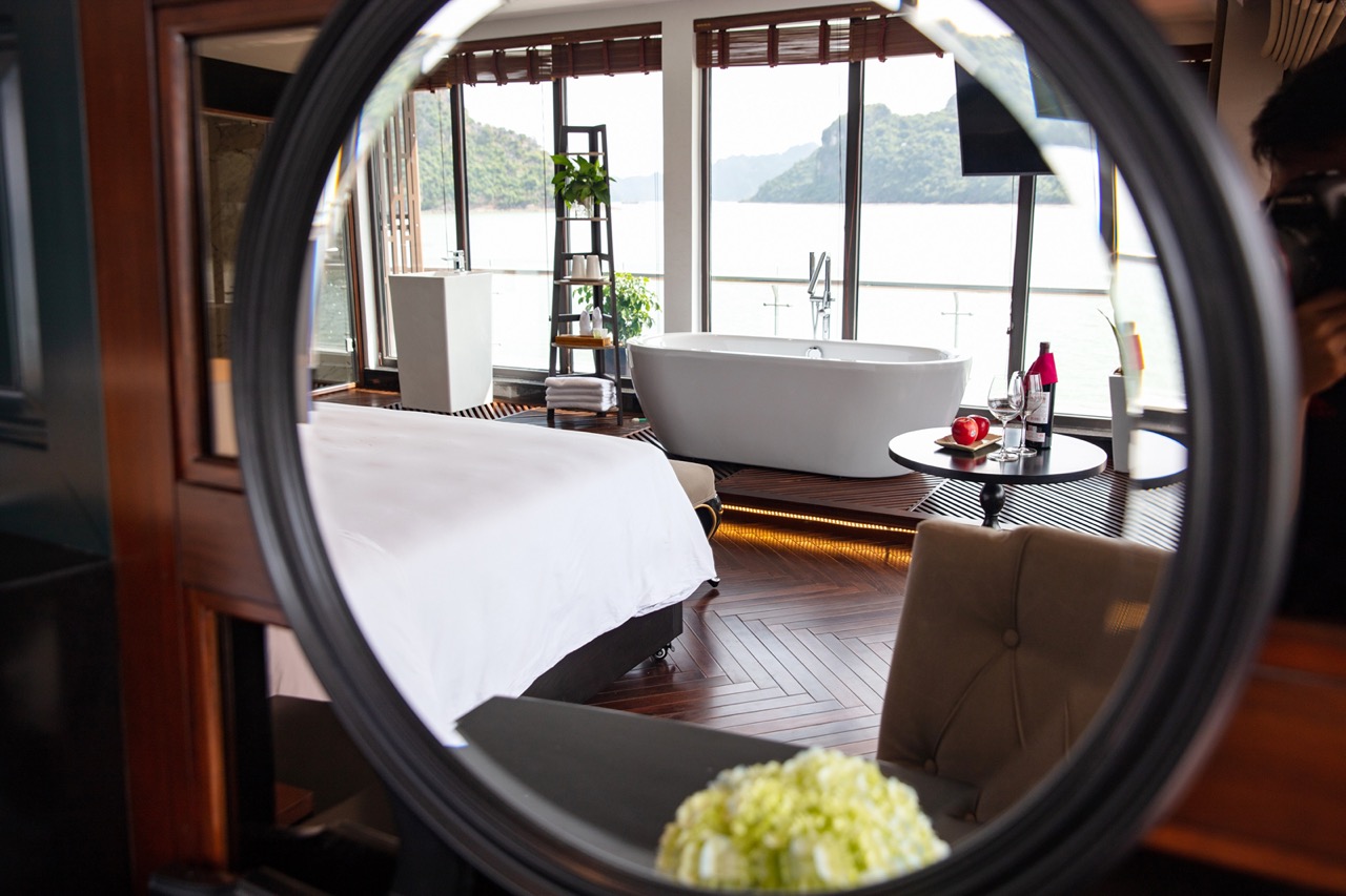 Luxurious lakeside hotel room with bathtub and panoramic view of mountains and water.