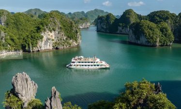 Stunning view of Lan Ha Bay with a cruise boat sailing through emerald waters surrounded by lush lim.