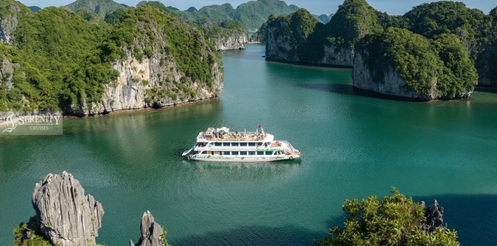 Stunning view of Lan Ha Bay with a cruise boat sailing through emerald waters surrounded by lush lim.