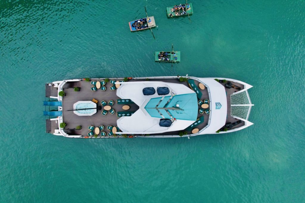 Aerial view of a luxurious catamaran cruising Lan Ha Bay with smaller boats nearby, showcasing a sce.
