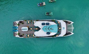 Aerial view of a luxurious catamaran cruising Lan Ha Bay with smaller boats nearby, showcasing a sce.