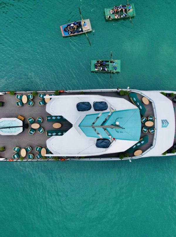 Aerial view of a luxurious catamaran cruising Lan Ha Bay with smaller boats nearby, showcasing a sce.
