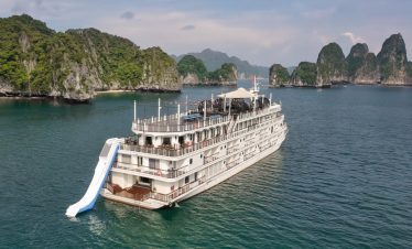A large white cruise ship sailing through Halong Bay with lush green islands in the background.