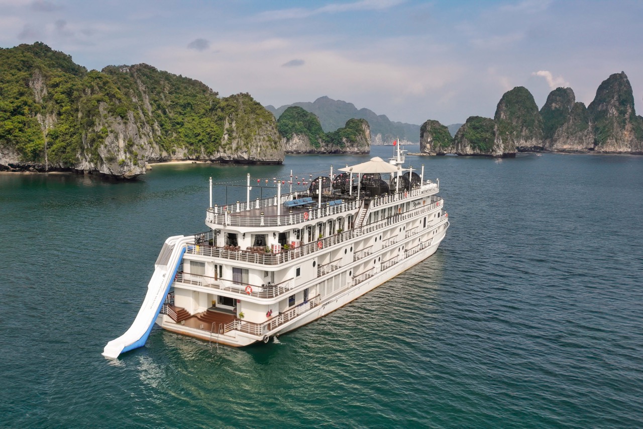 A large white cruise ship sailing through Halong Bay with lush green islands in the background.