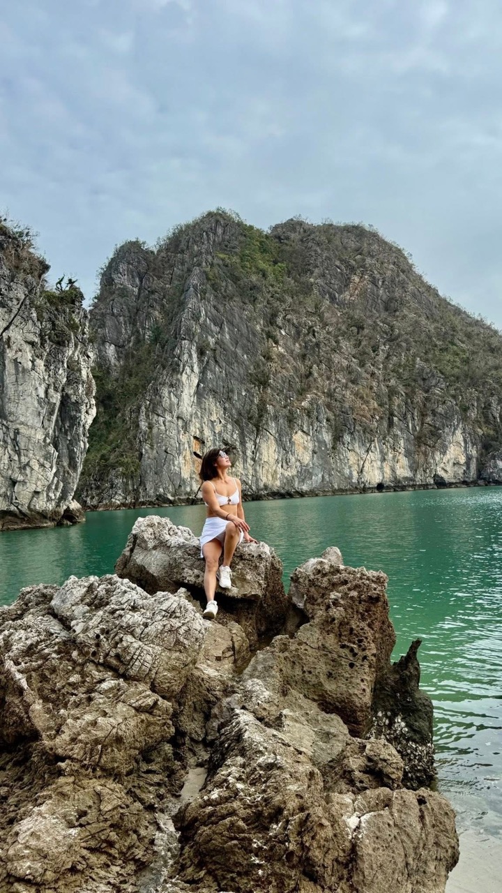 Stunning woman sitting on rocks by emerald water in Halong Bay, Vietnam.
