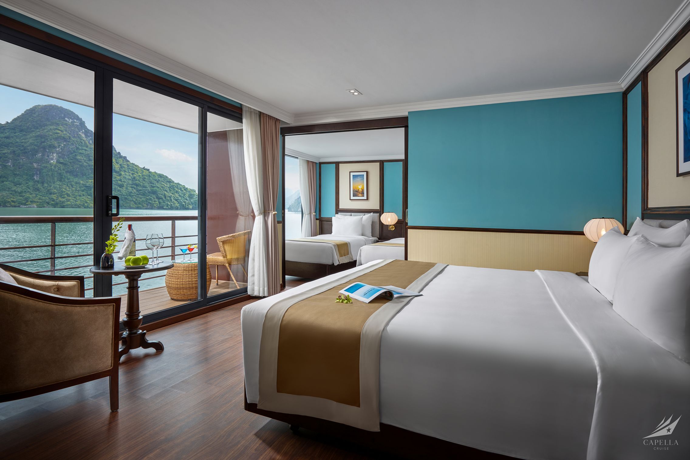 Elegant hotel room with balcony view of lush mountains and water, modern decor, and comfortable beds.
