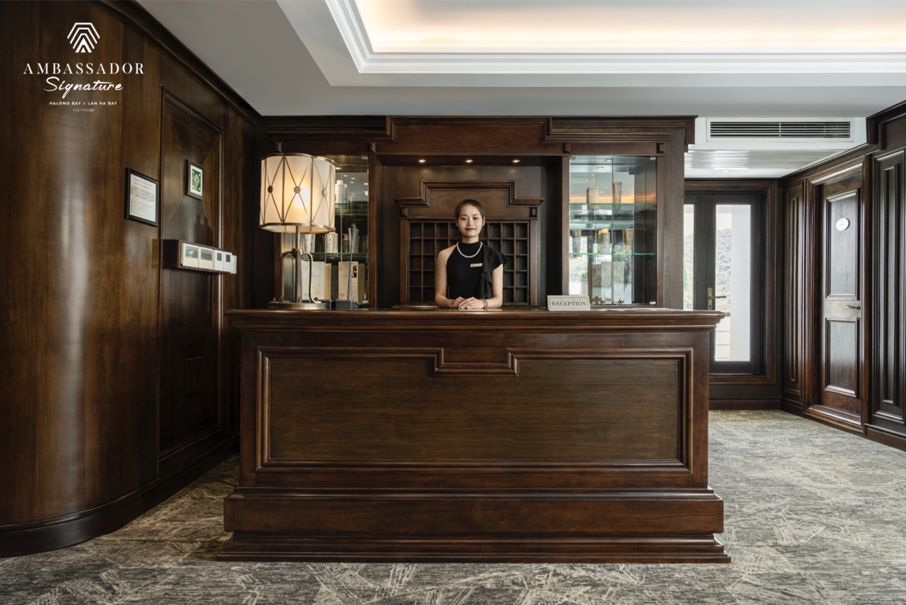 Elegant cruise reception with wooden decor and welcoming staff in Halong Bay.