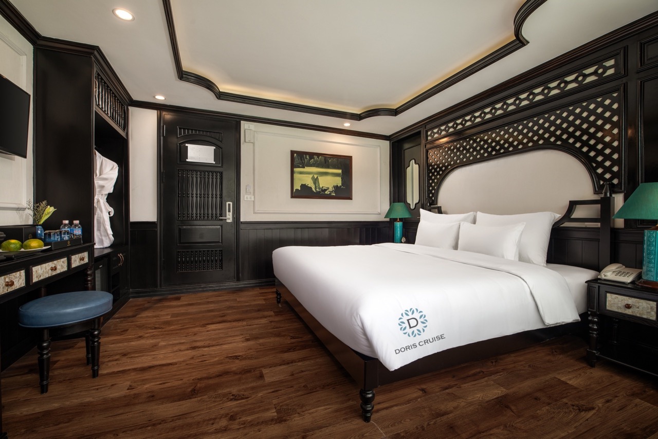 A luxurious bedroom aboard a Halong Bay cruise with elegant dark wood furnishings and a cozy, inviti.