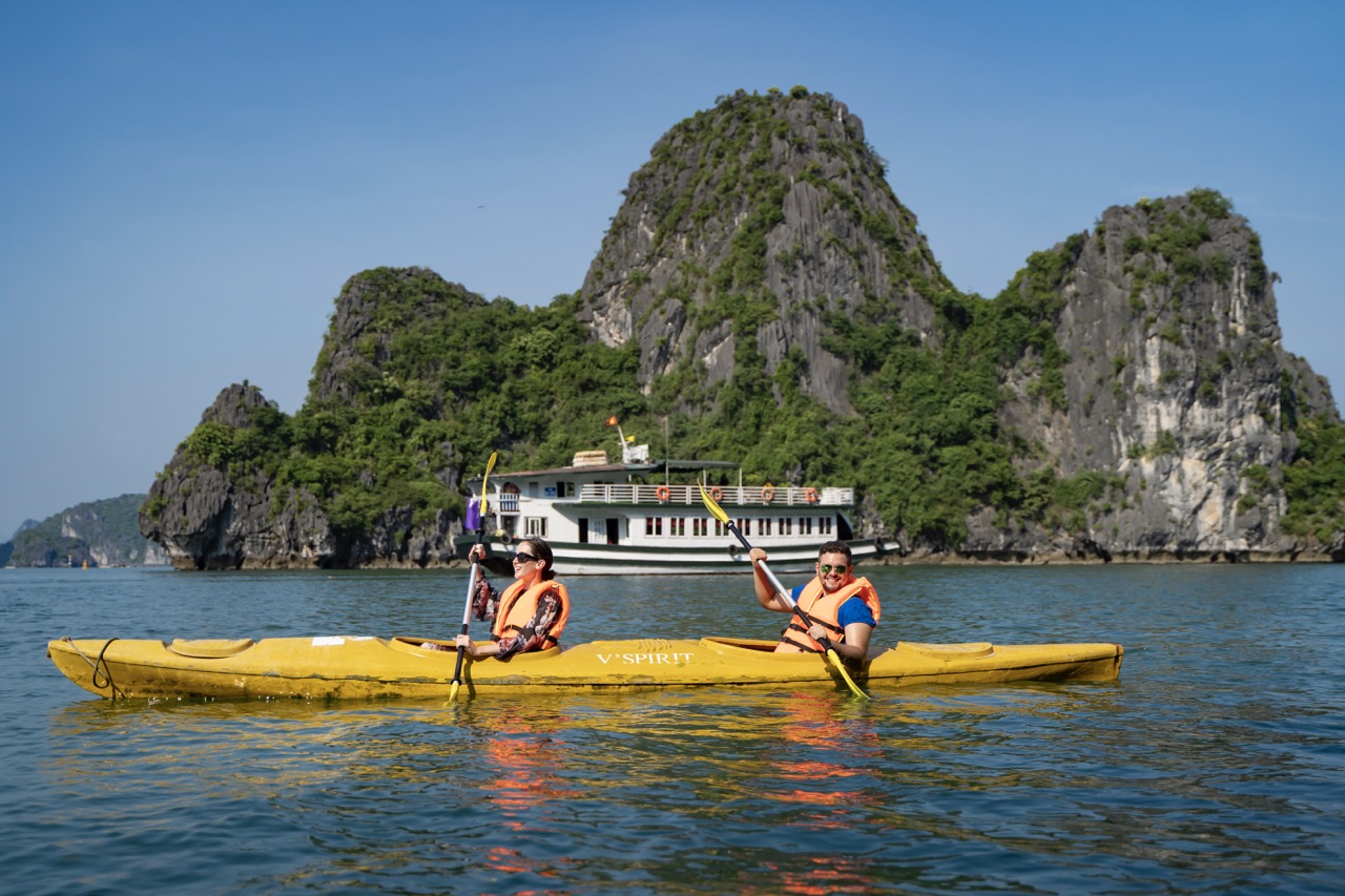Kayakers enjoying the scenic Halong Bay tour in Vietnam with limestone karsts and boat cruises.