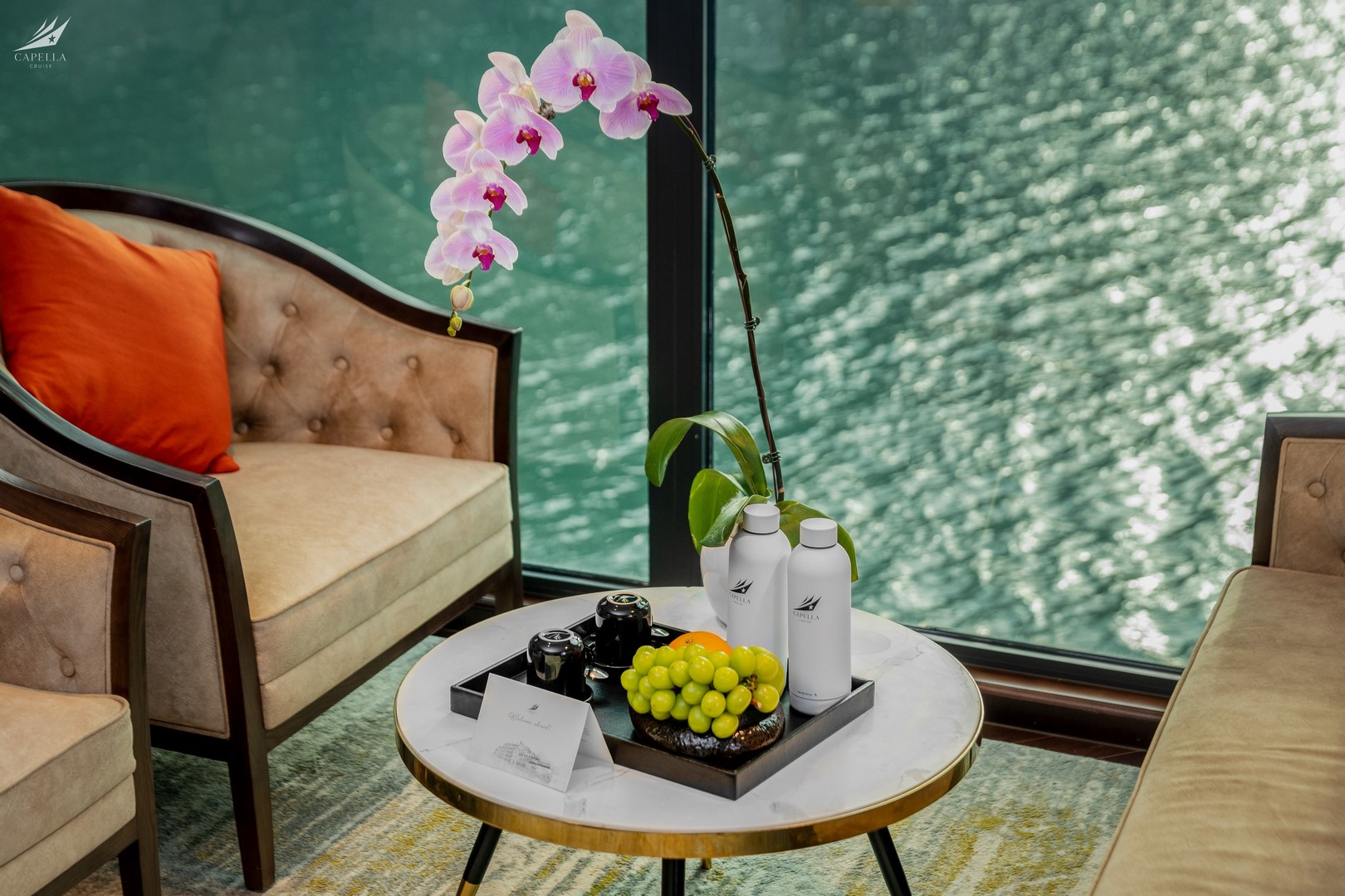 Elegant hotel lounge with a water view, featuring orchids, plush seating, and refreshing beverages for a luxurious experience.