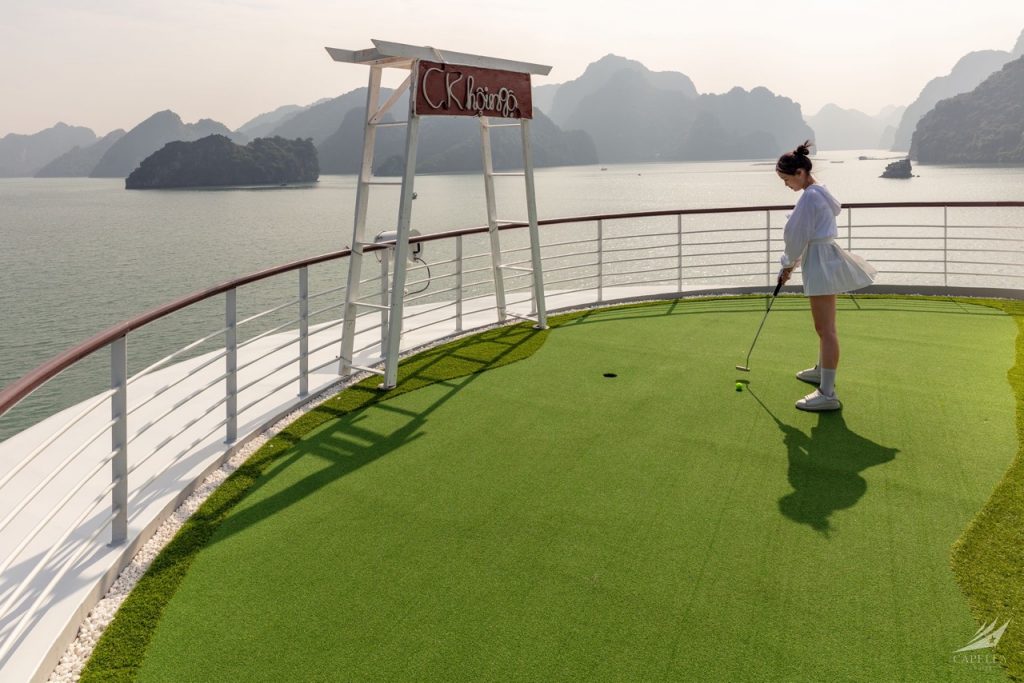 A girl playing mini golf on a scenic outdoor course overlooking a bay with limestone islands.