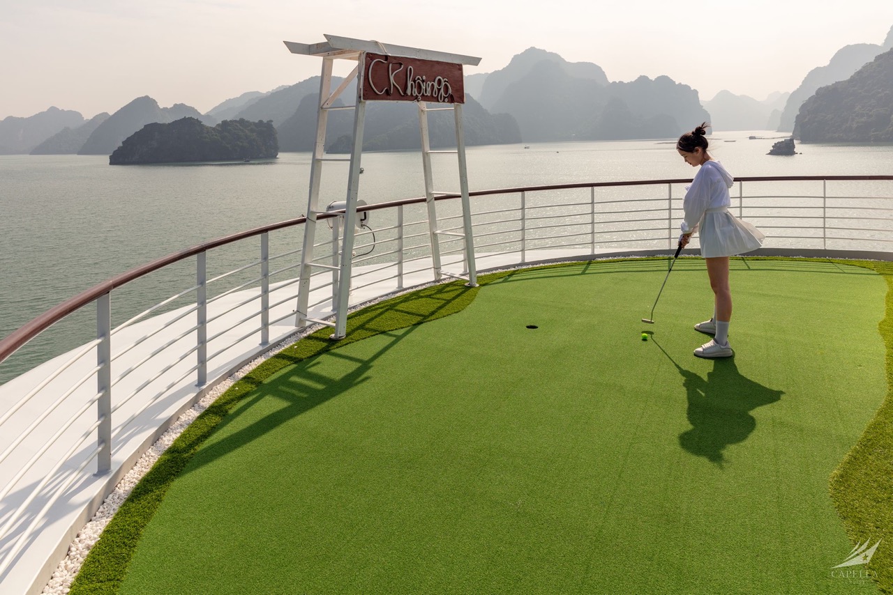 A girl playing mini golf on a scenic outdoor course overlooking a bay with limestone islands.