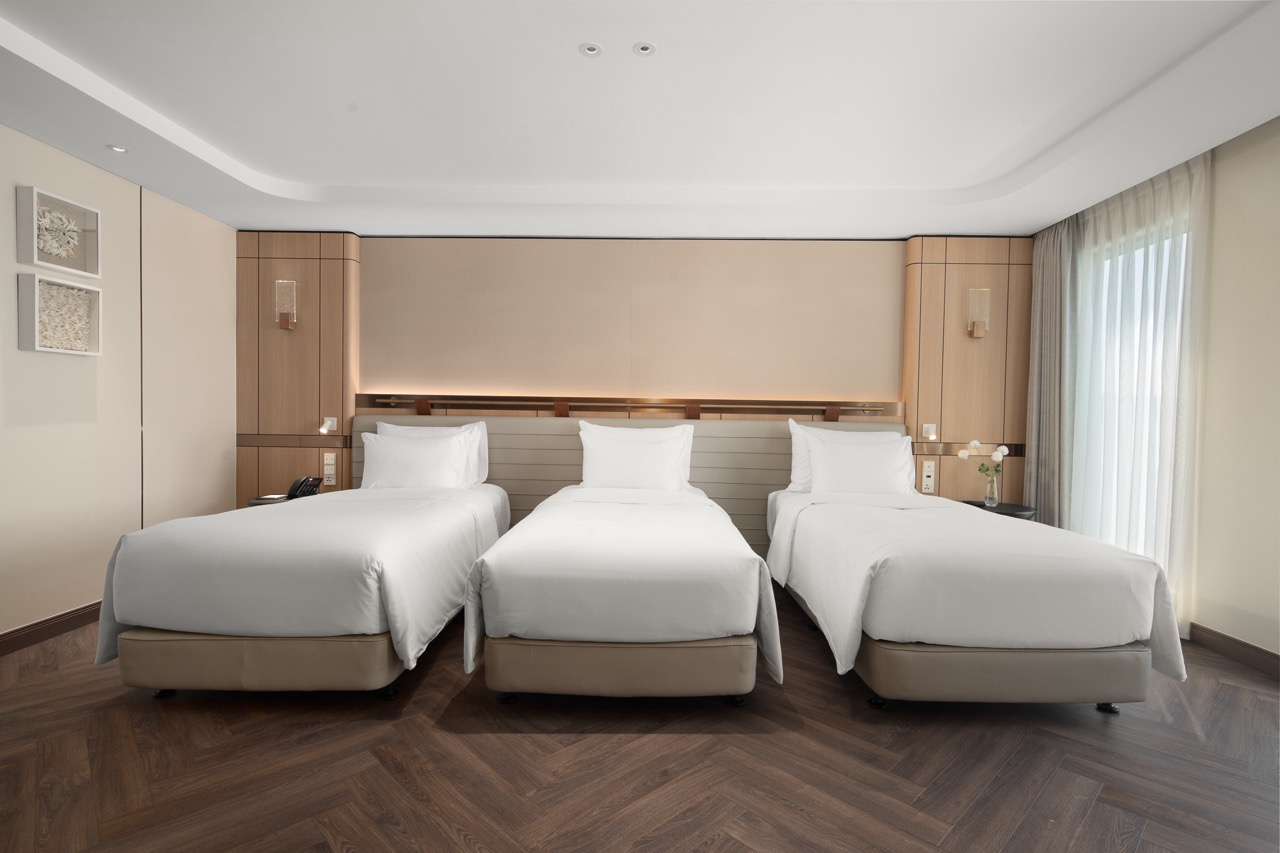 Modern hotel room with three neatly made beds and cozy decor, perfect for relaxation and comfort.