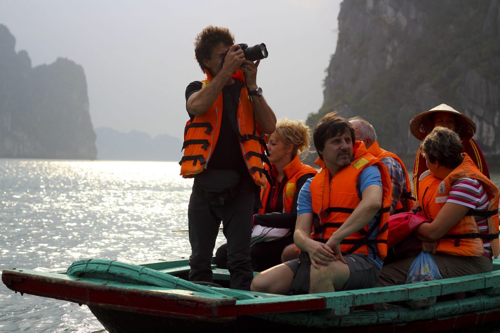 An Asian woman taking photos of tourists on a boat tour in Ha Long Bay, Vietnam.