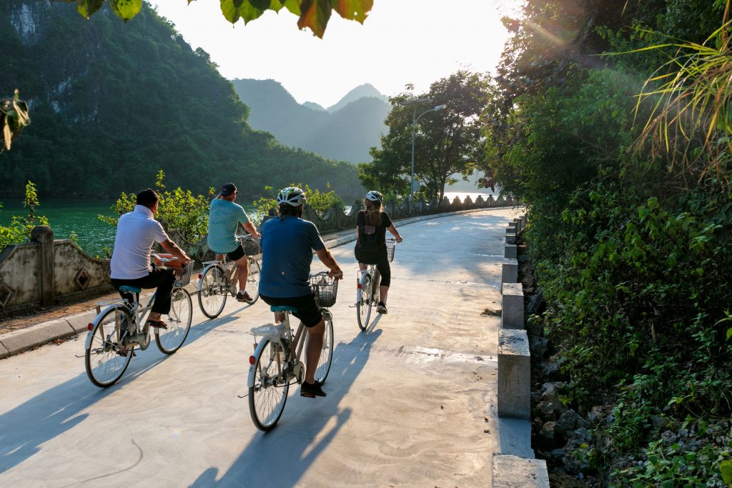Bicyclists enjoying scenic countryside tour along river in Vietnam during sunny day.