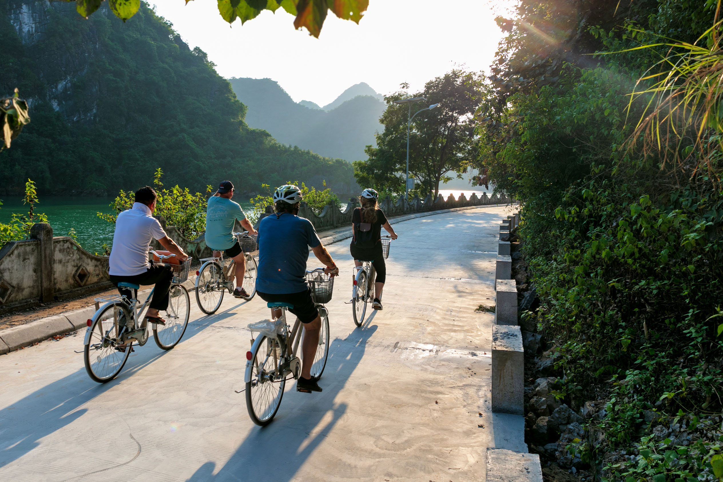 Bicyclists enjoying scenic countryside tour along river in Vietnam during sunny day.