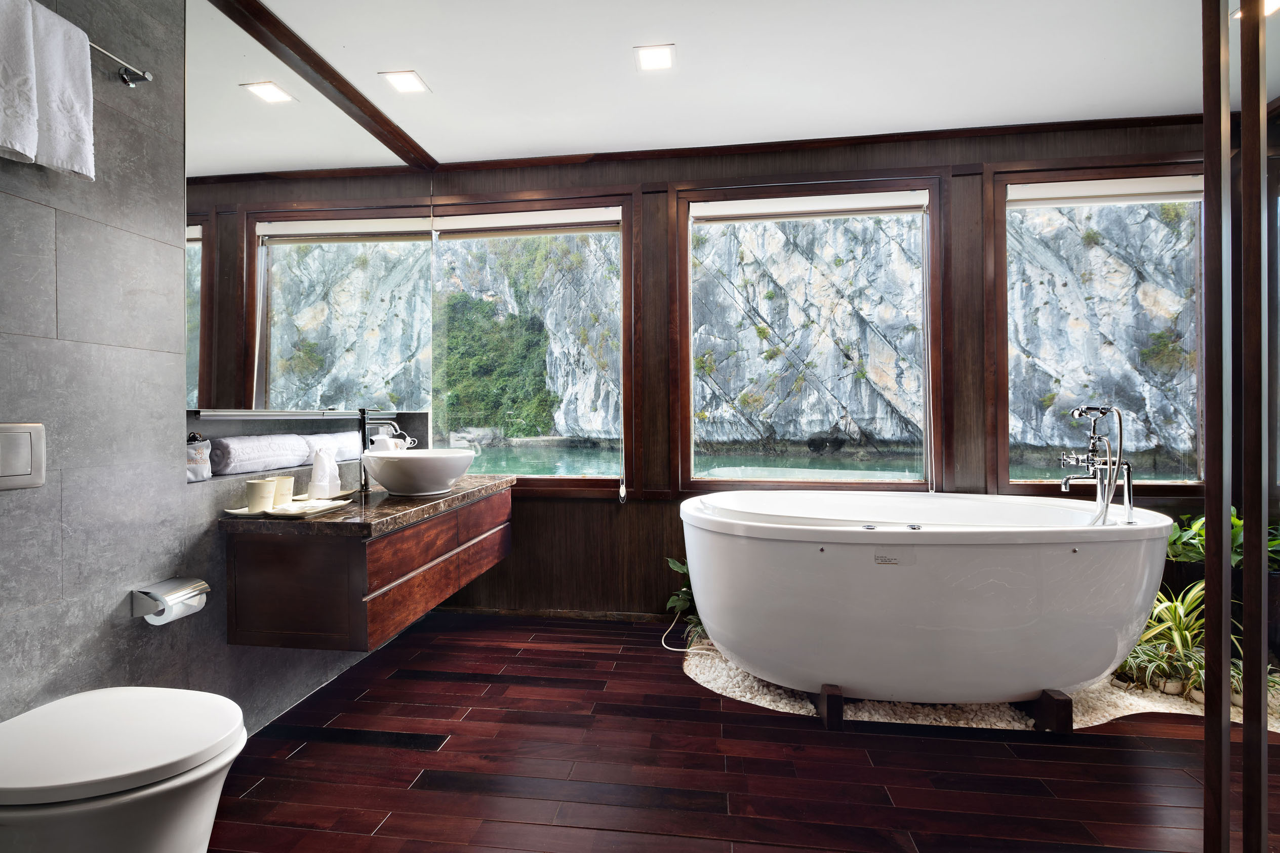 Luxury bathroom with river view and tub at a villa in Vietnam, wooden accents, modern fixtures, and natural scenery outside.