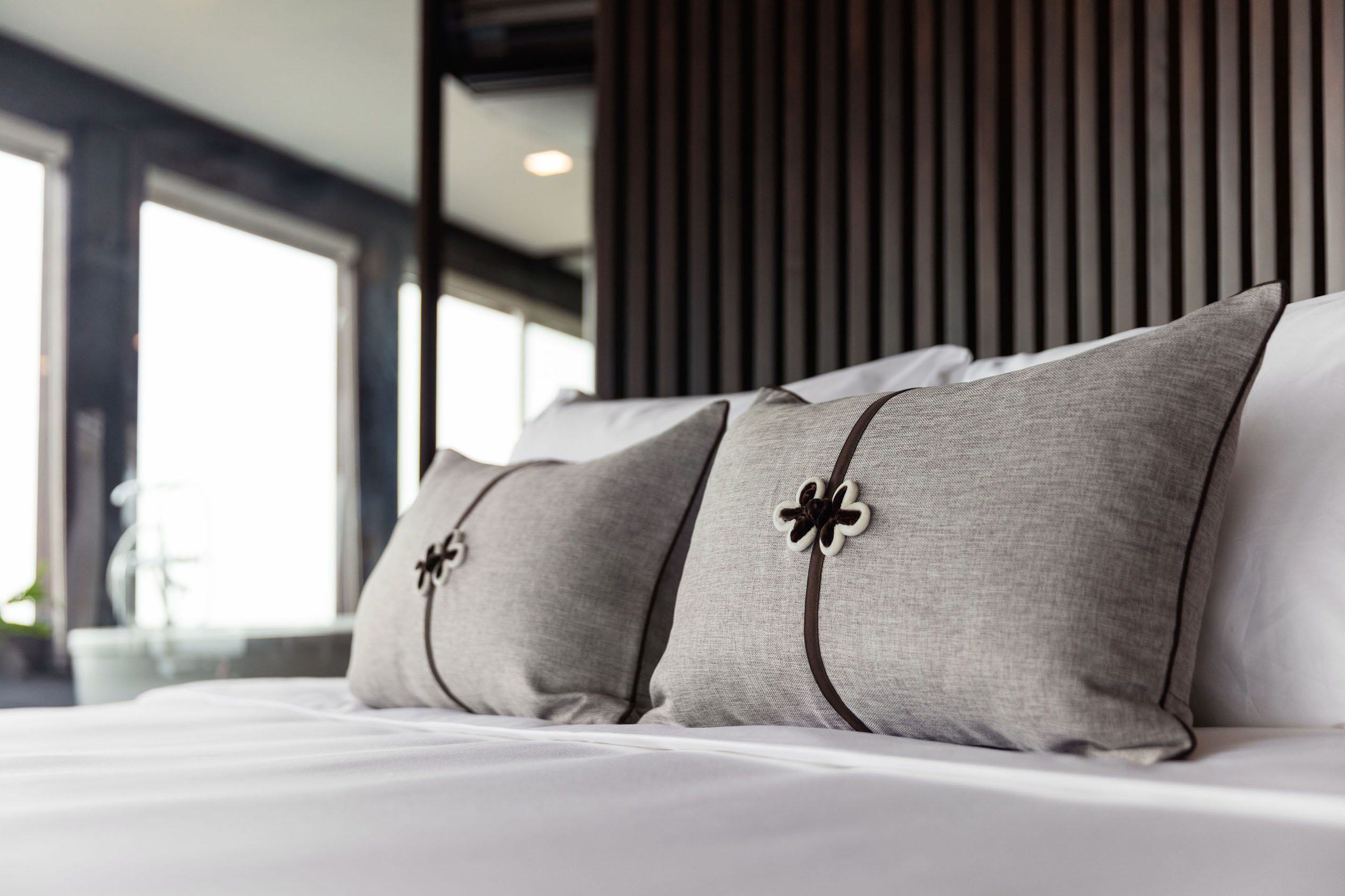 Luxurious hotel bed with grey decorative pillows and modern interior design, perfect for a relaxing stay.