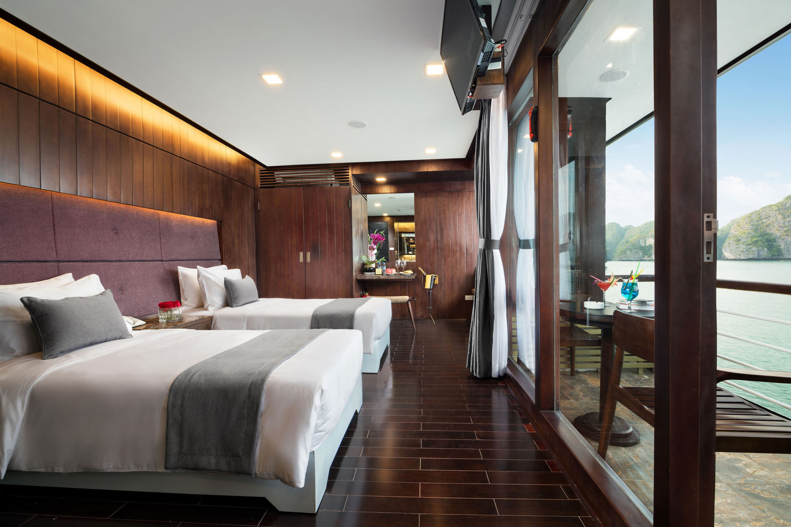 Luxurious hotel room with sea view, modern decor, and balcony overlooking emerald waters and mountainous landscape.
