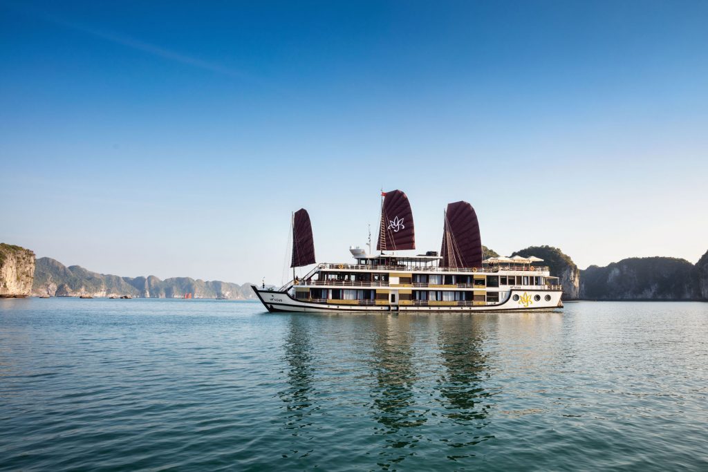 Luxury cruise boat sailing through Halong Bay, Vietnam at sunset.