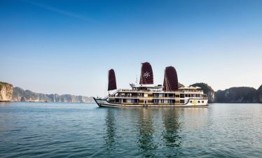 Luxury cruise boat sailing through Halong Bay, Vietnam at sunset.