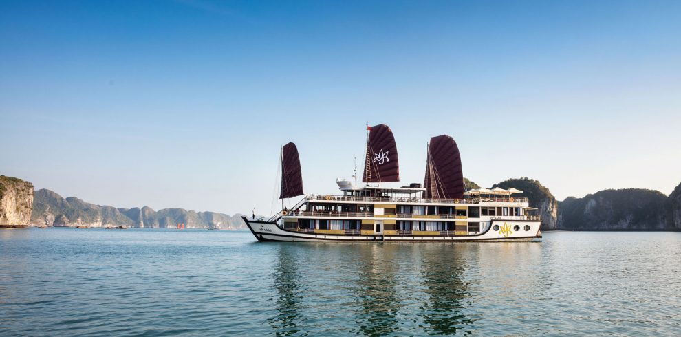 Luxury cruise boat sailing through Halong Bay, Vietnam at sunset.